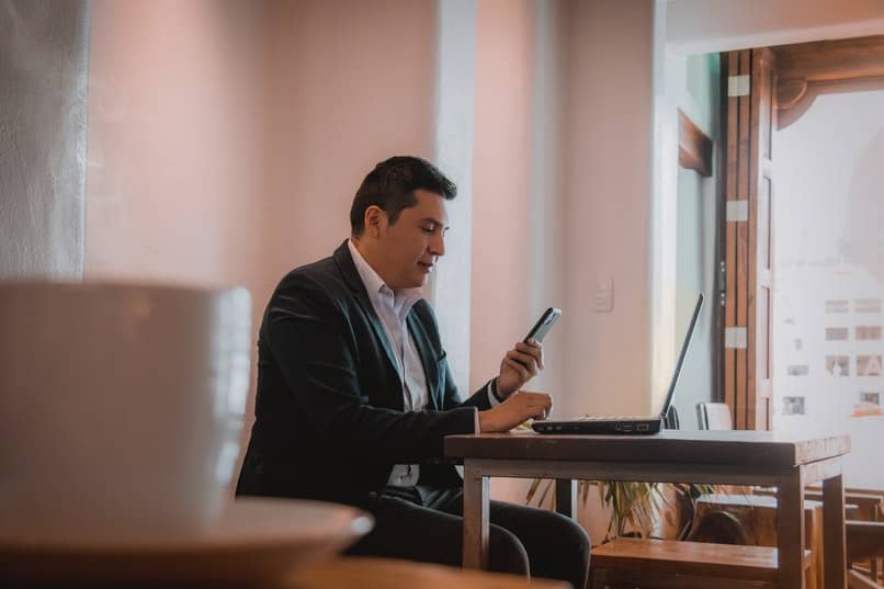 hombre en una oficia con un celular y una pc abierta