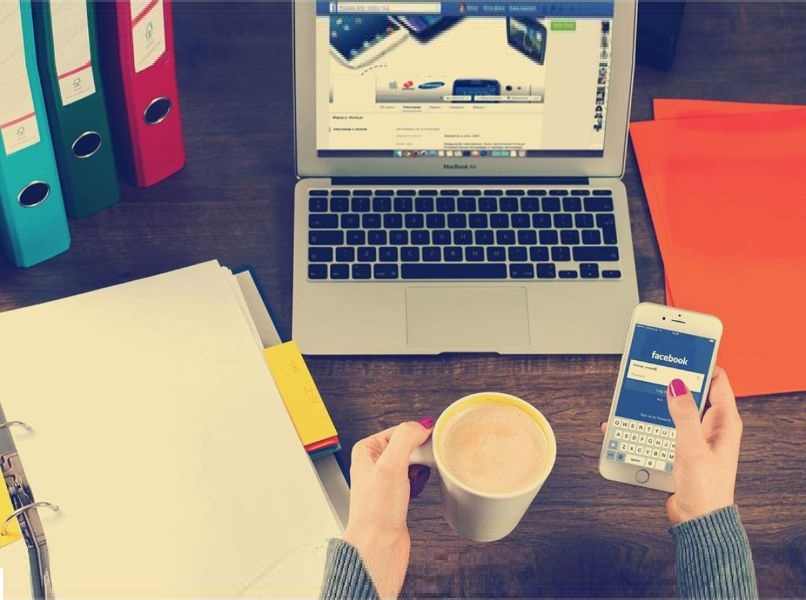 taza cafe movil manos persona escritorio madera oscura latop gris carpetas coloridas